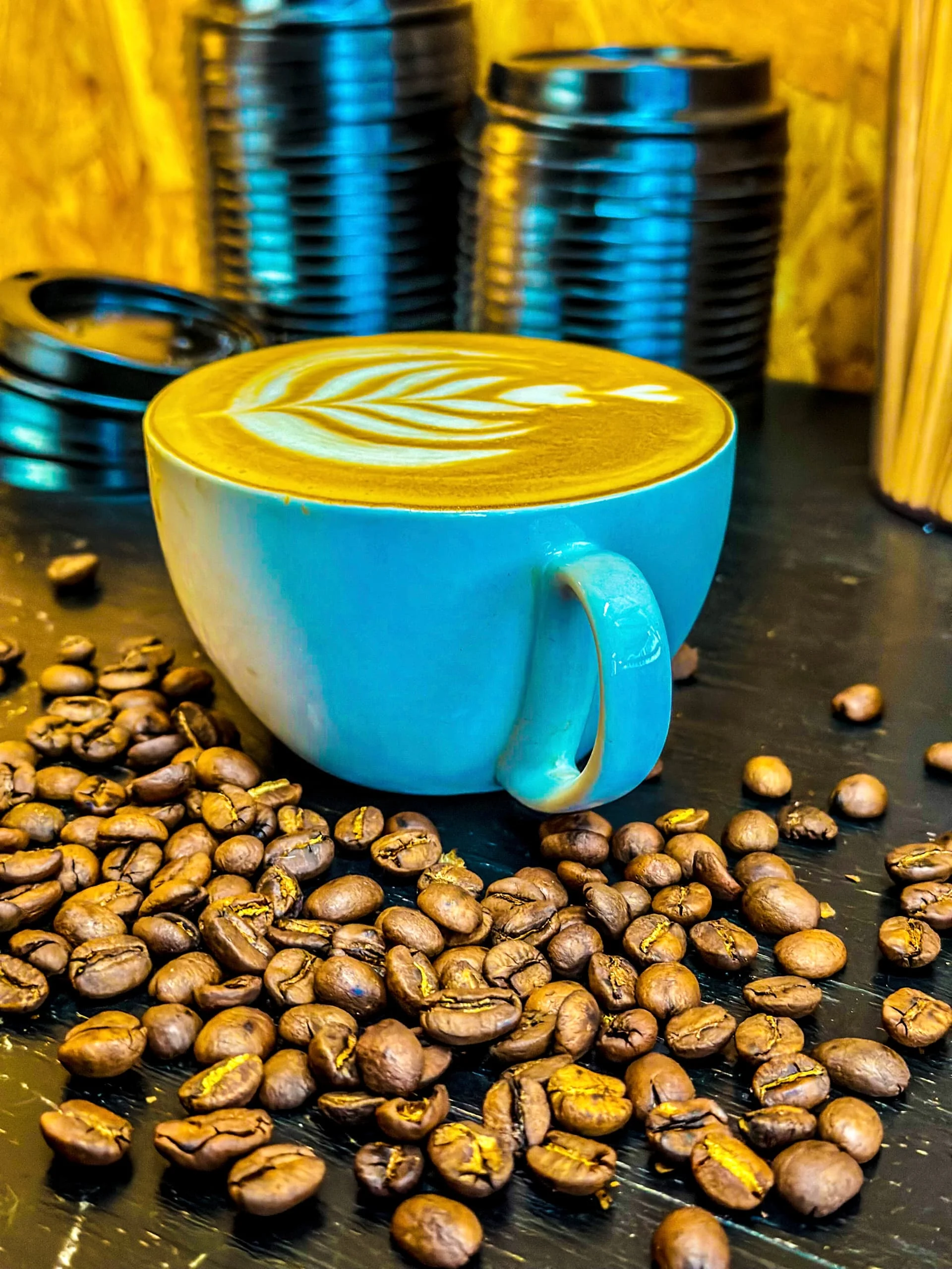 EL-J Coffee dramatic latte in vibrant blue cup surrounded by roasted beans