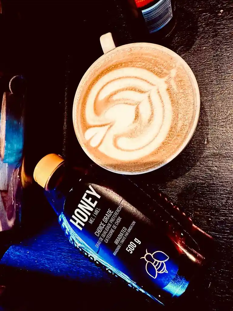 Latte art next to a jar of honey on a dark surface
